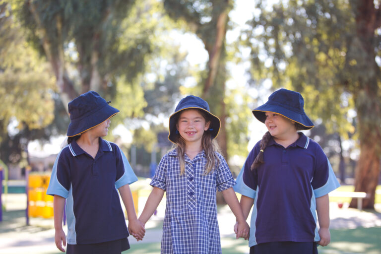 Three primary school students stand holding hats with sun safe hats on.