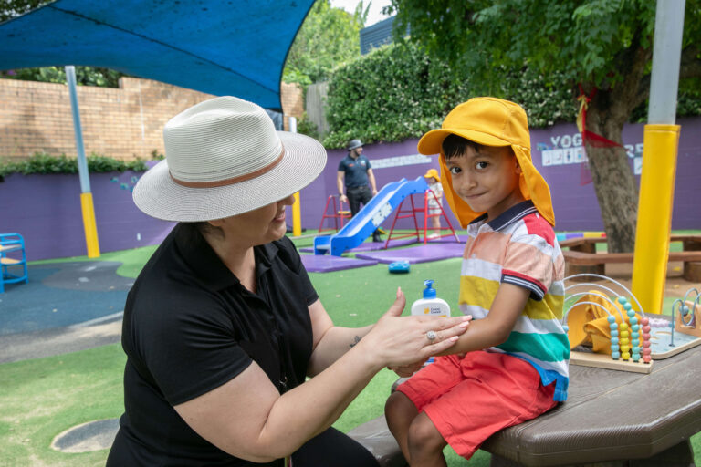 An early childhood educator applies sunscreen to the arm of a child.